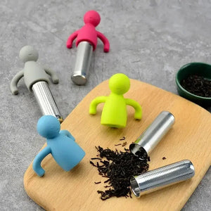 Colorful silicone tea infusers on a wooden board with loose tea leaves.