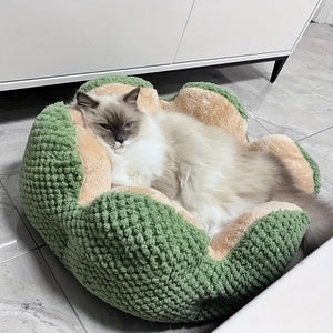 Long-haired cat resting inside a green flower-shaped plush pet bed on a tiled floor.