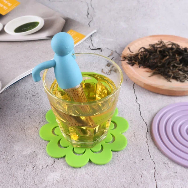Tea infuser in a glass of tea with a coaster on a gray surface
