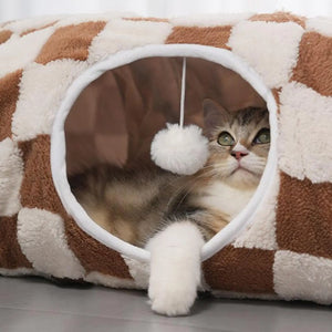 Cat resting inside a brown and white donut cat tunnel cave bed with hanging plush toy ball, soft velvet indoor cat bed