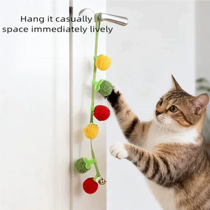 Cat playing with tomato and persimmon cat teaser string toy with bell hanging from a door handle, interactive self‑play cat toy for indoor cats.
