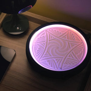 Round LED zen sand lamp with intricate geometric sand pattern glowing pink on a wooden desk beside a lamp and phone